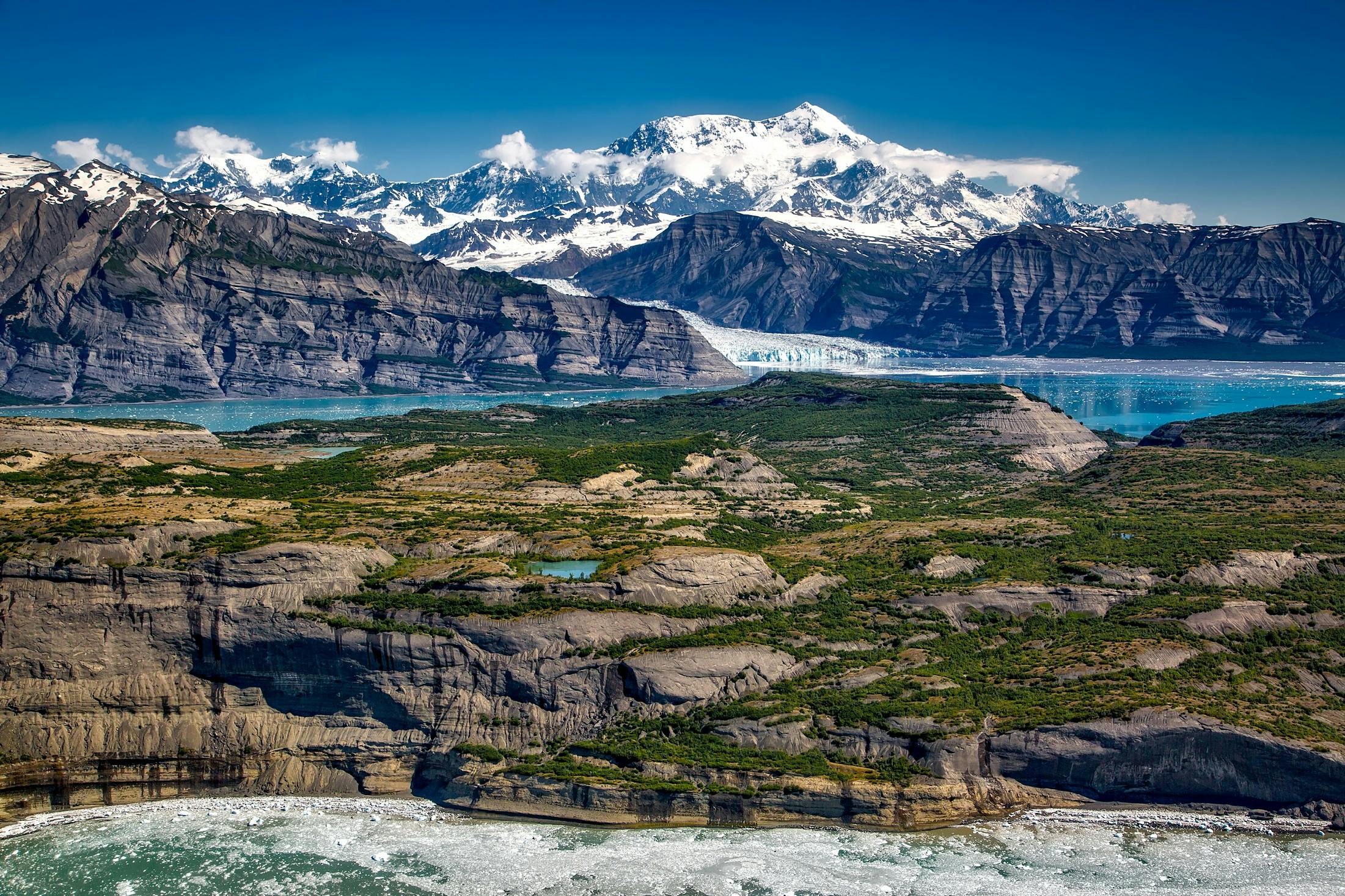 Breathtaking view of Alaskan mountains with glacier and lake, capturing nature's serene beauty.